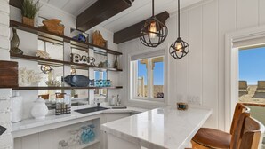 Una cocina con muebles blancos, una isla de mármol, sillas de madera e iluminación colgante.