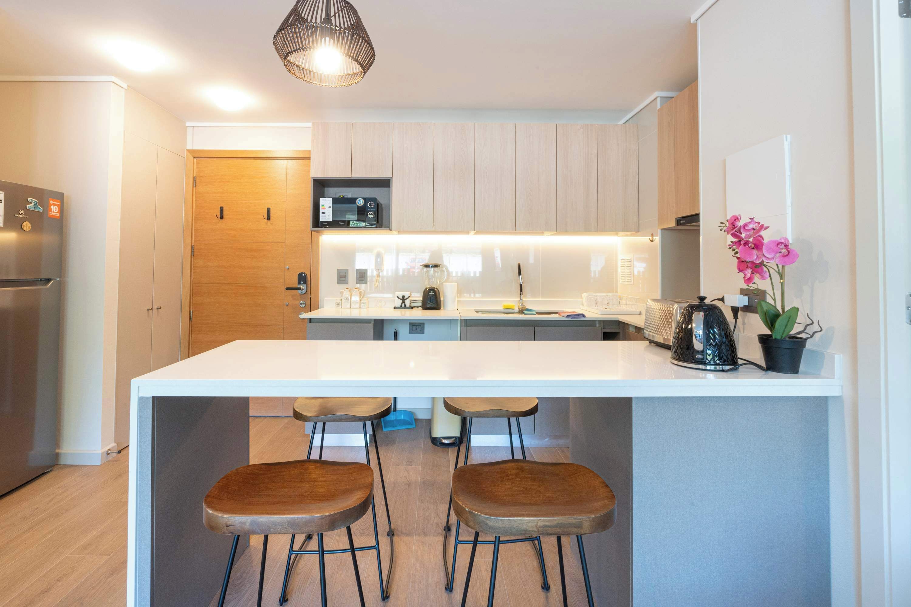 A modern kitchen with a central island, bar stools, a microwave, and a potted plant.