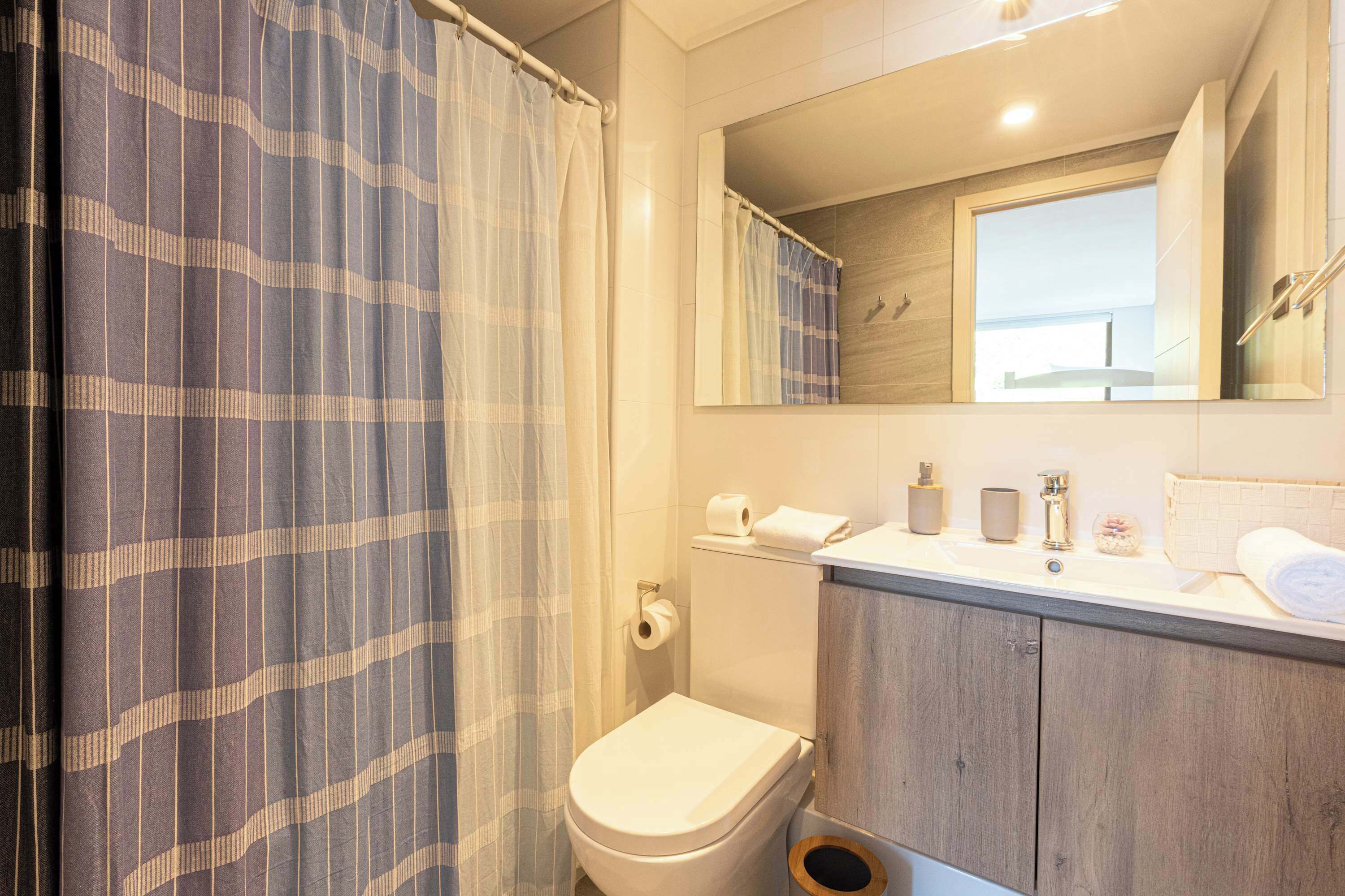 A bathroom with a toilet, a sink, a mirror, and a shower curtain.