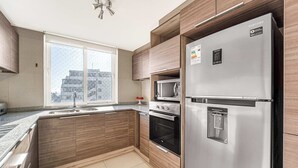 A modern kitchen with a stainless steel refrigerator, built-in oven, microwave, and a window with a view of buildings. - Costa Vina 3B  Balcony & View (Viña del Mar)