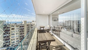 A balcony with a table and chairs, a glass railing, and a view of other buildings. - Costa Vina 3B  Balcony & View (Viña del Mar)