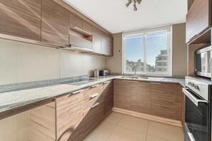 Cocina moderna con armarios de madera, encimera de granito, horno de acero inoxidable y ventana con vista a la ciudad.