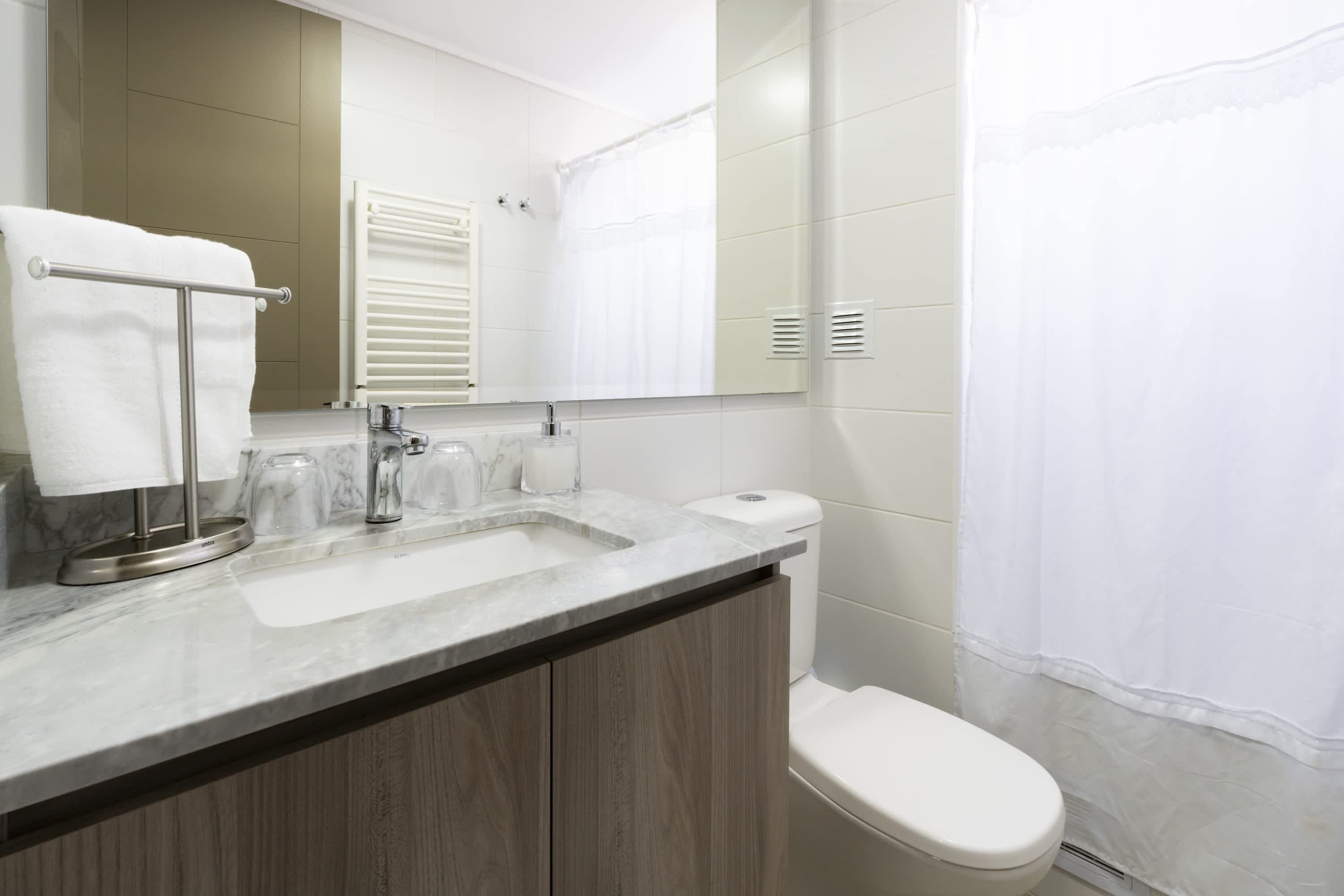 Ein modernes Badezimmer mit Marmorwaschtisch, Holzschränken, Toilette und Duschvorhang.
