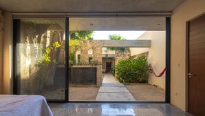 Une chambre moderne dotée d’une porte-fenêtre coulissante donnant sur une cour intérieure agrémentée d’un mur en pierre, de plantes et d’un sentier.