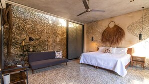 Une chambre avec un mur en pierre, un lit avec une literie blanche, un canapé foncé et un ventilateur de plafond.