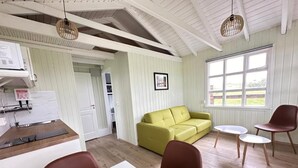 A room with a kitchen, a dining area with a table and chairs, a yellow sofa, and a window with a view of the outdoors. - Cave Cabins (Rangárþing ytra)