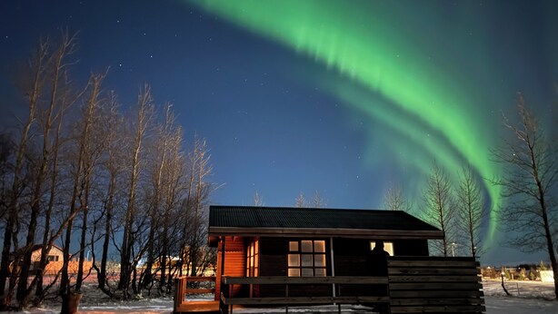A cabin with a wooden exterior, a porch, and a window overlooking a snowy landscape. - Cave Cabins (Rangárþing ytra)