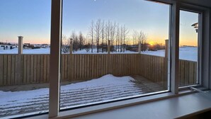 A room with a large window overlooking a snowy outdoor area with a wooden fence and trees. - Cave Cabins (Rangárþing ytra)