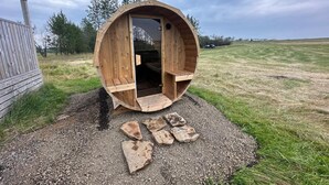 A wooden barrel-shaped structure with an open door, surrounded by gravel and grass. - Cave Cabins (Rangárþing ytra)