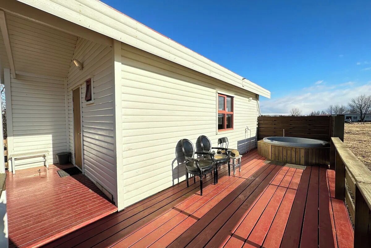 A white single-story house with a wooden deck, a hot tub, and two chairs.