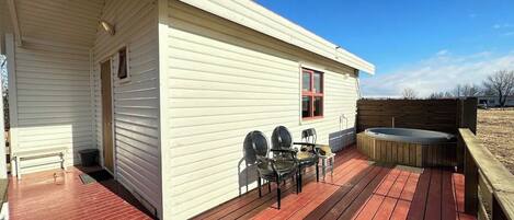 A white single-story house with a wooden deck, a hot tub, and two chairs.