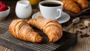 Un tavolo di legno con croissant, una tazza di caffè e una piccola ciotola di lamponi.