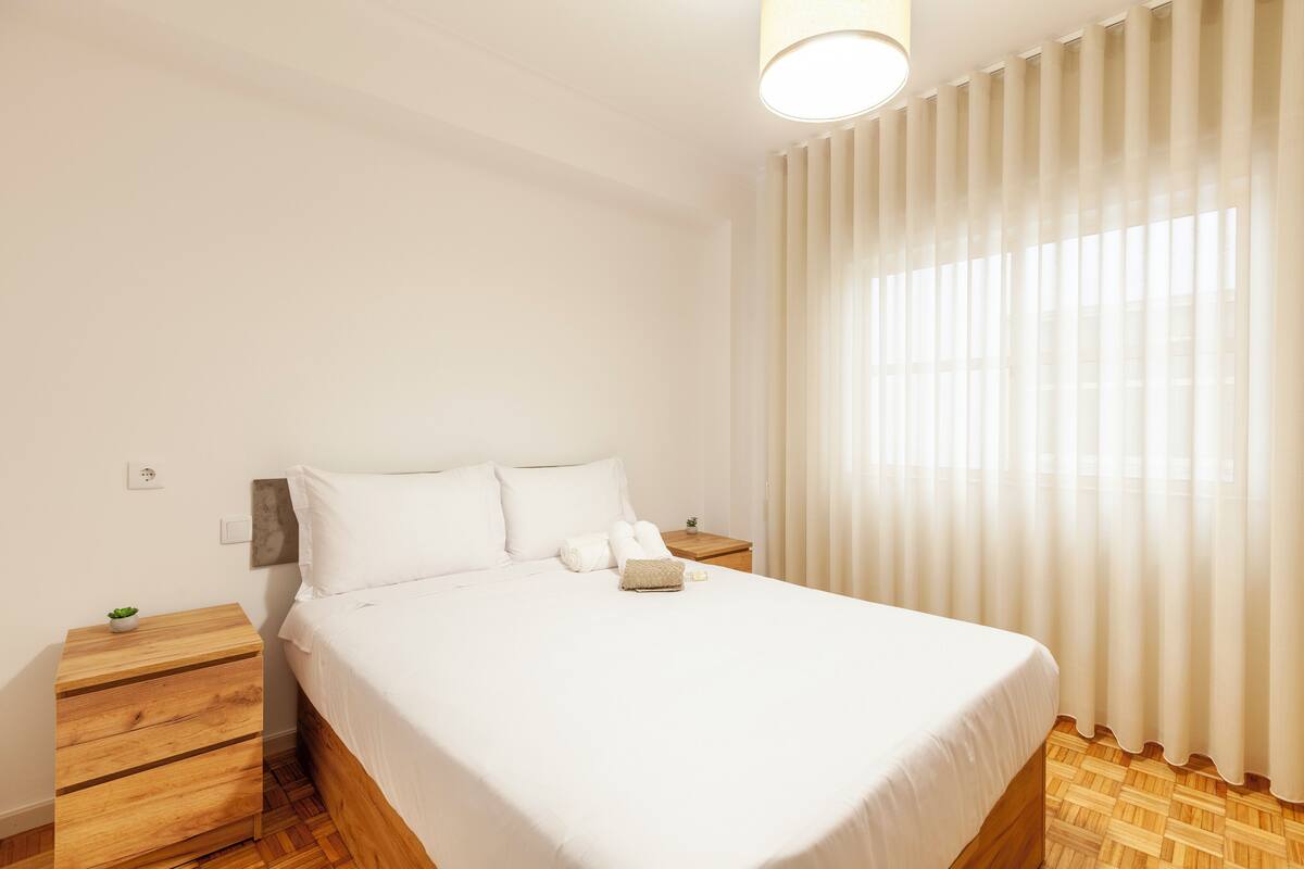 Un dormitorio ordenado con cama, mesitas de noche de madera y una planta pequeña.