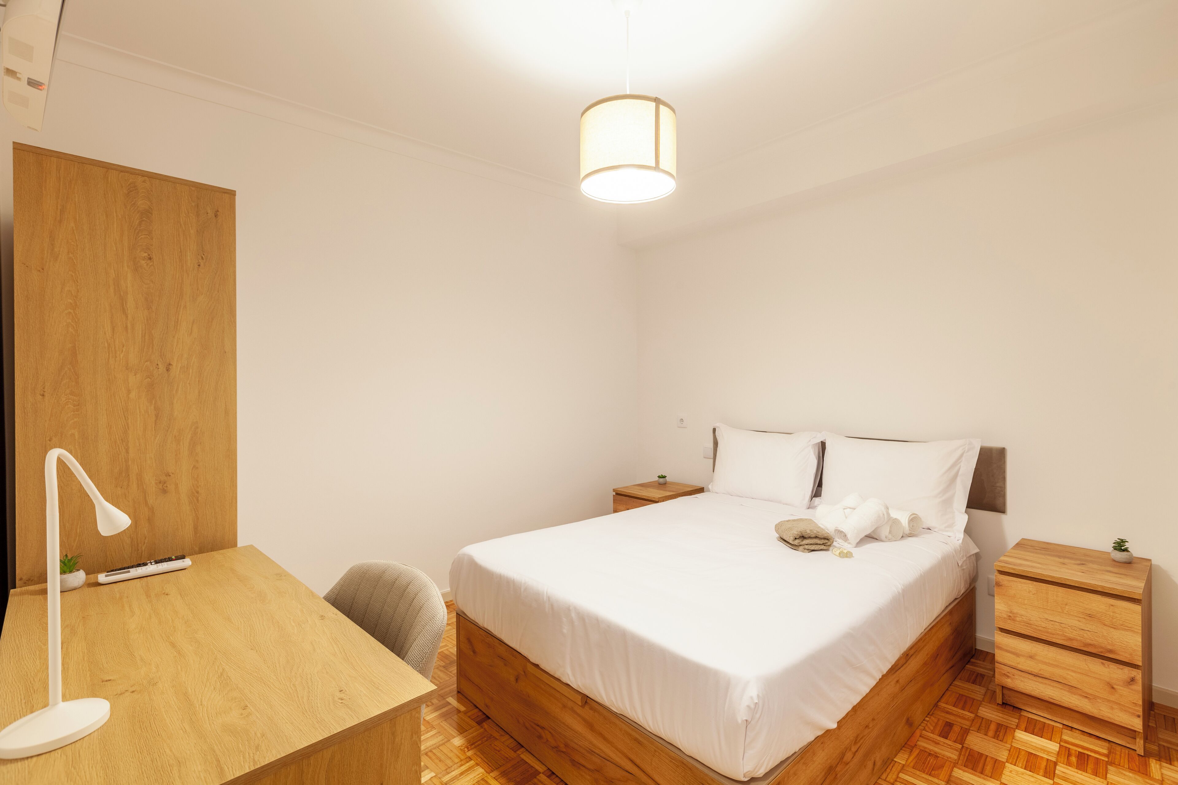 Une chambre à coucher avec un lit en bois, un bureau avec une lampe, une table de chevet et un luminaire suspendu.
