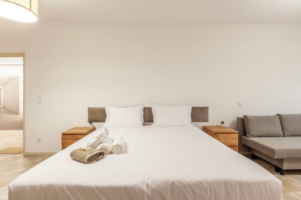 Una habitación de hotel con una cama grande, dos mesitas de noche, un sofá y una pequeña mesa con toallas.