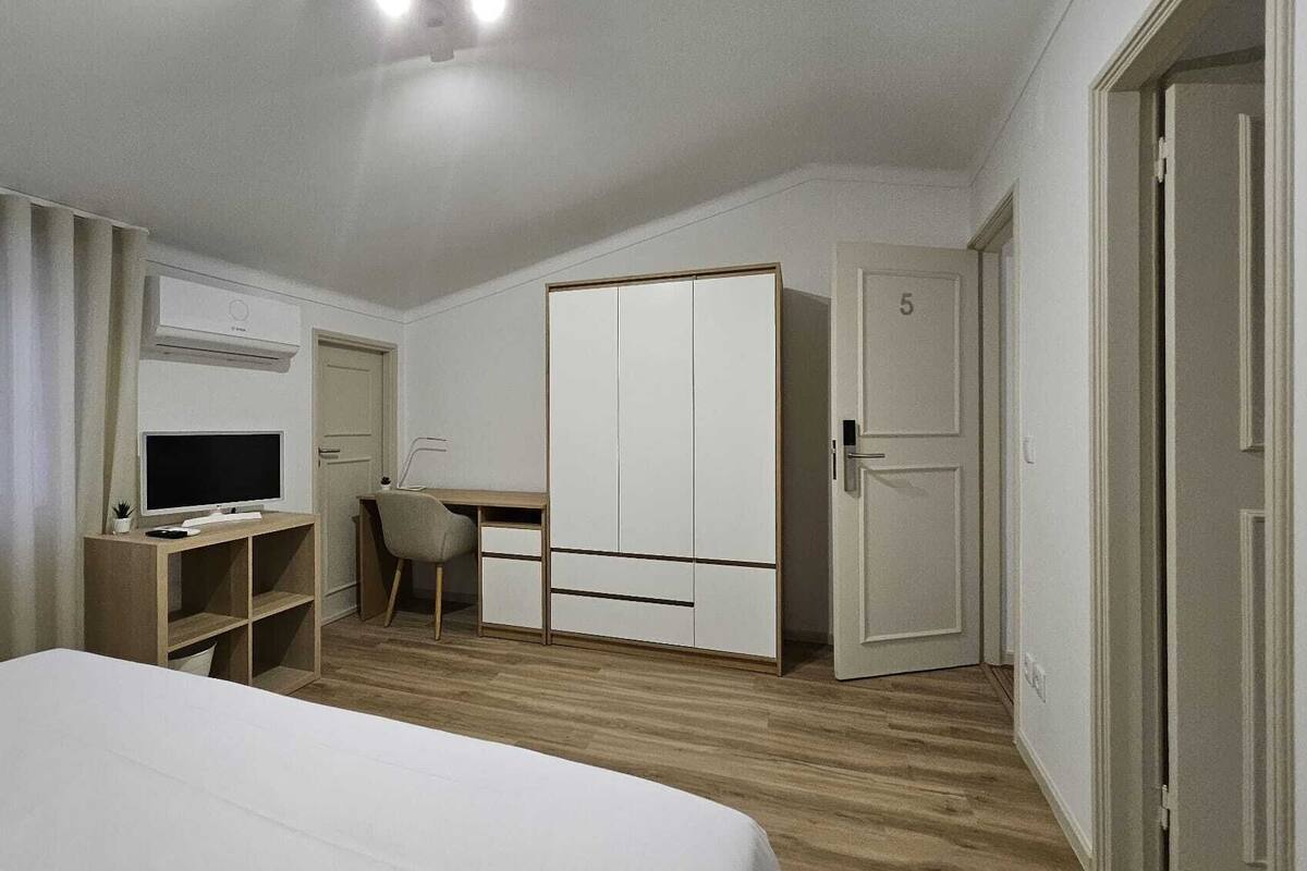 Un dormitorio con una cama, un escritorio con computadora, una silla, un armario y una puerta.