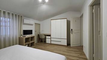 A bedroom with a bed, a desk with a computer, a chair, a wardrobe, and a door.