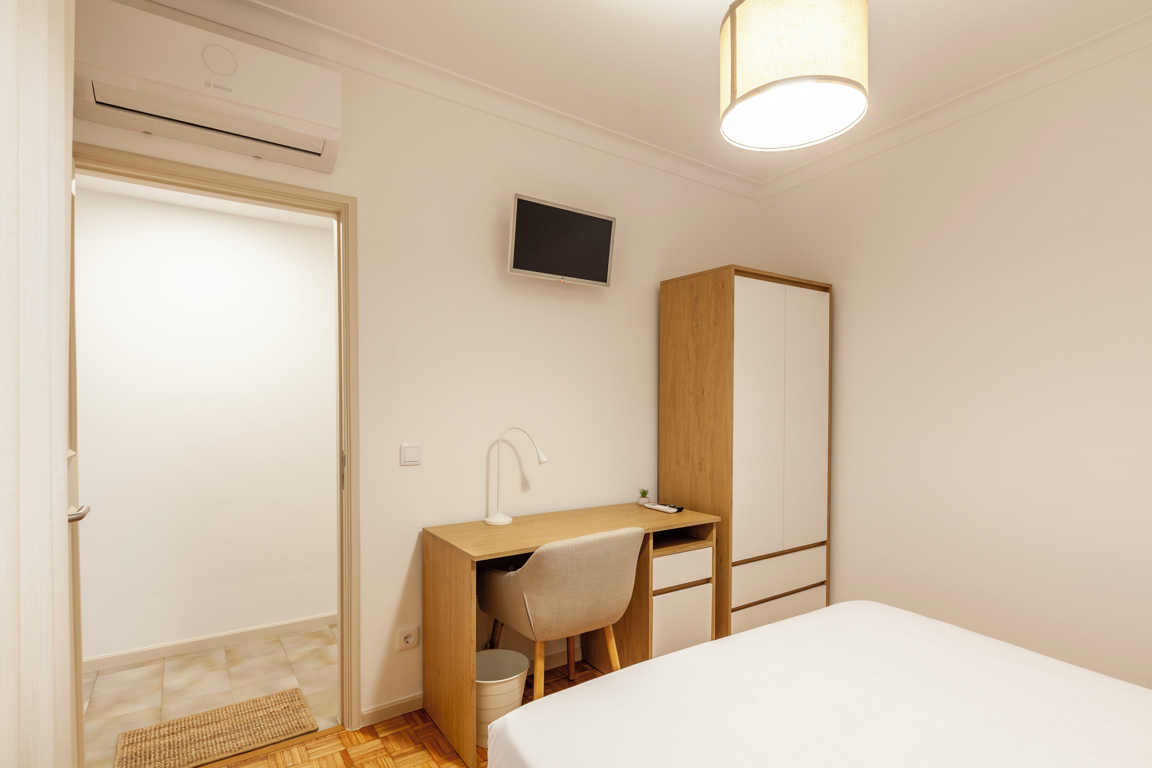 Un dormitorio con cama, escritorio, silla, televisor y armario.