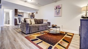 A living room with a grey sofa, a coffee table, and a patterned rug. There is a kitchen in the background with cabinets and a microwave. - GLOBALSTAY New Basement 4Bd in Port Elgin. Close to the Beach (Port Elgin/Canada)