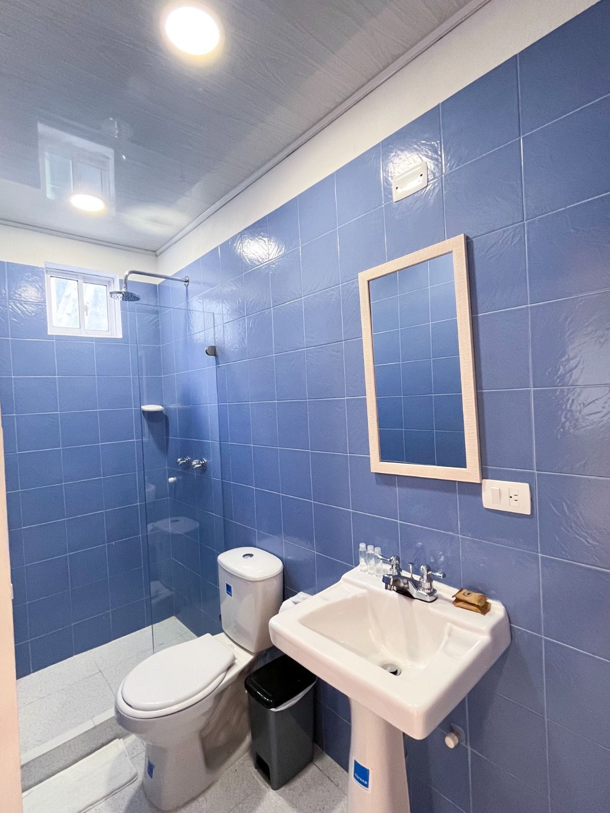 A bathroom with blue tiles, a white sink, a toilet, and a shower.