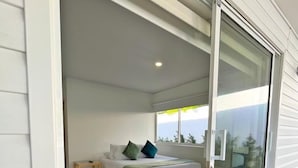 A bedroom with a bed, pillows, a bedside table, and a view through a sliding glass door. - Zaba Beach House (San Andrés)
