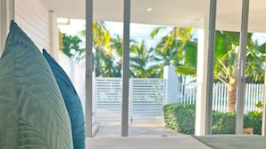 A modern room with a large sliding glass door leading to a balcony with a view of palm trees and a white fence. - Zaba Beach House (San Andrés)