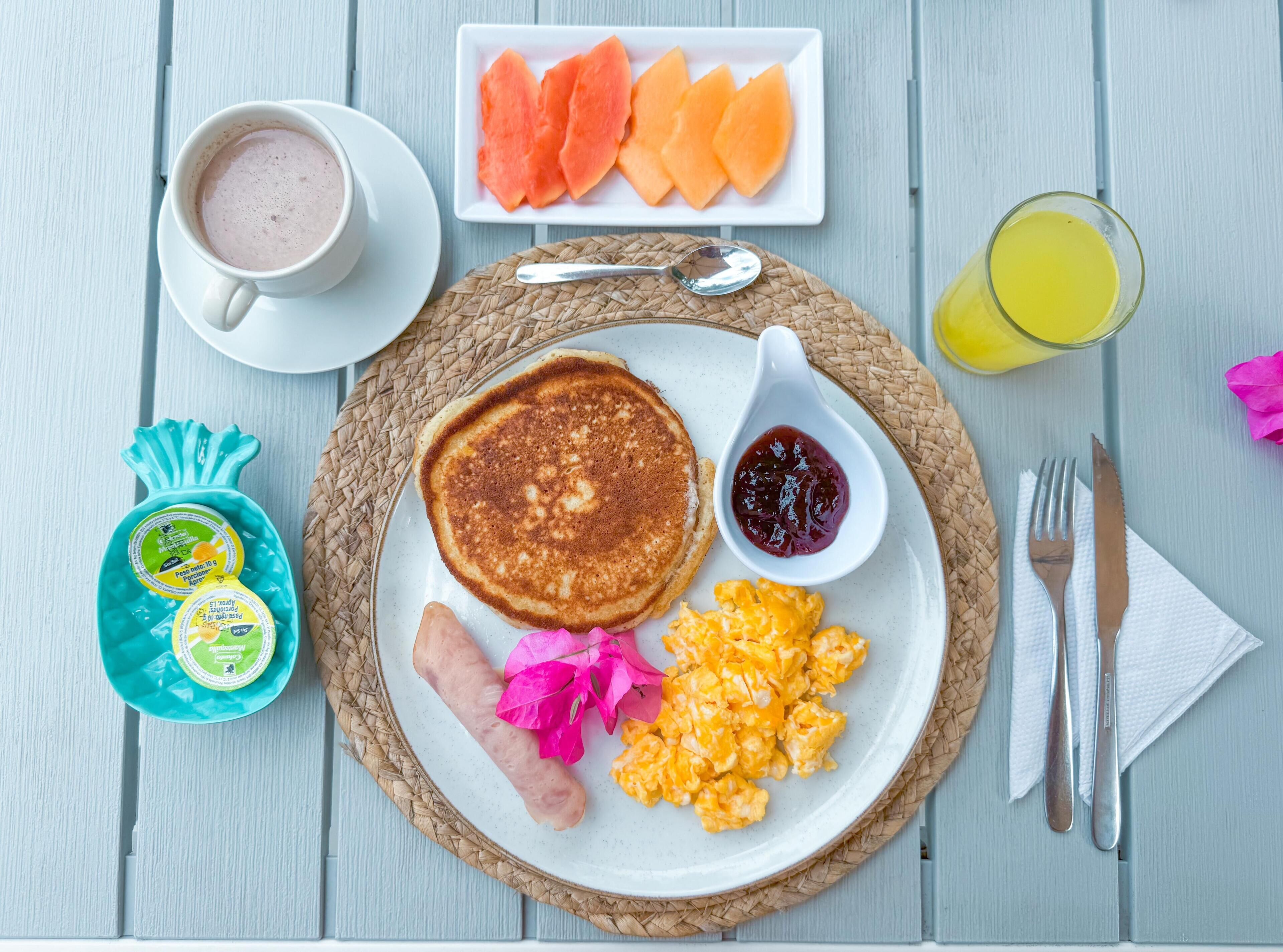 A breakfast plate with pancakes, sausage, scrambled eggs, and a side of fruit.