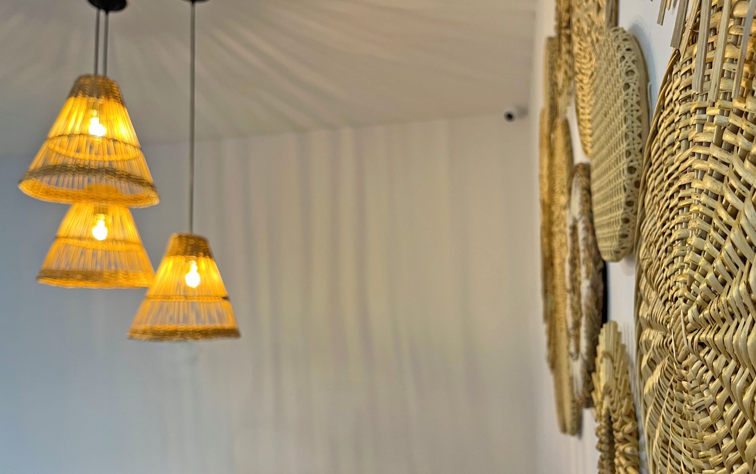 Three hanging lamps with a woven design, a white tent-like structure, and a wall with woven baskets.