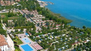 An aerial view of a coastal residential area with multiple small houses, a large swimming pool, and a beach in the background.
