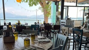 A restaurant with tables set for dining, a view of the lake, and a tree in the background.