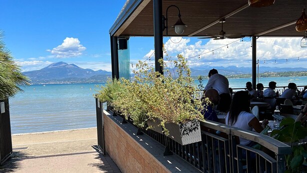 Terras met uitzicht op een meer en bergen, met tuinmeubelen en plantenpotten.