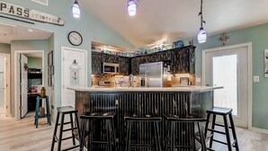 A kitchen with a central island, bar stools, and a clock on the wall. - Blue Heaven -  First Responders discount-  4 bedroom, 2 bath, sleeps 15. (Crystal Beach)