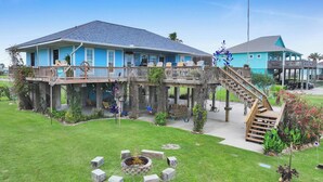 A two-story house with a deck, a fire pit, and a staircase leading to a second level. - Blue Heaven -  First Responders discount-  4 bedroom, 2 bath, sleeps 15. (Crystal Beach)