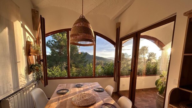 A dining area with a large wooden table, woven placemats, and a hanging light fixture.