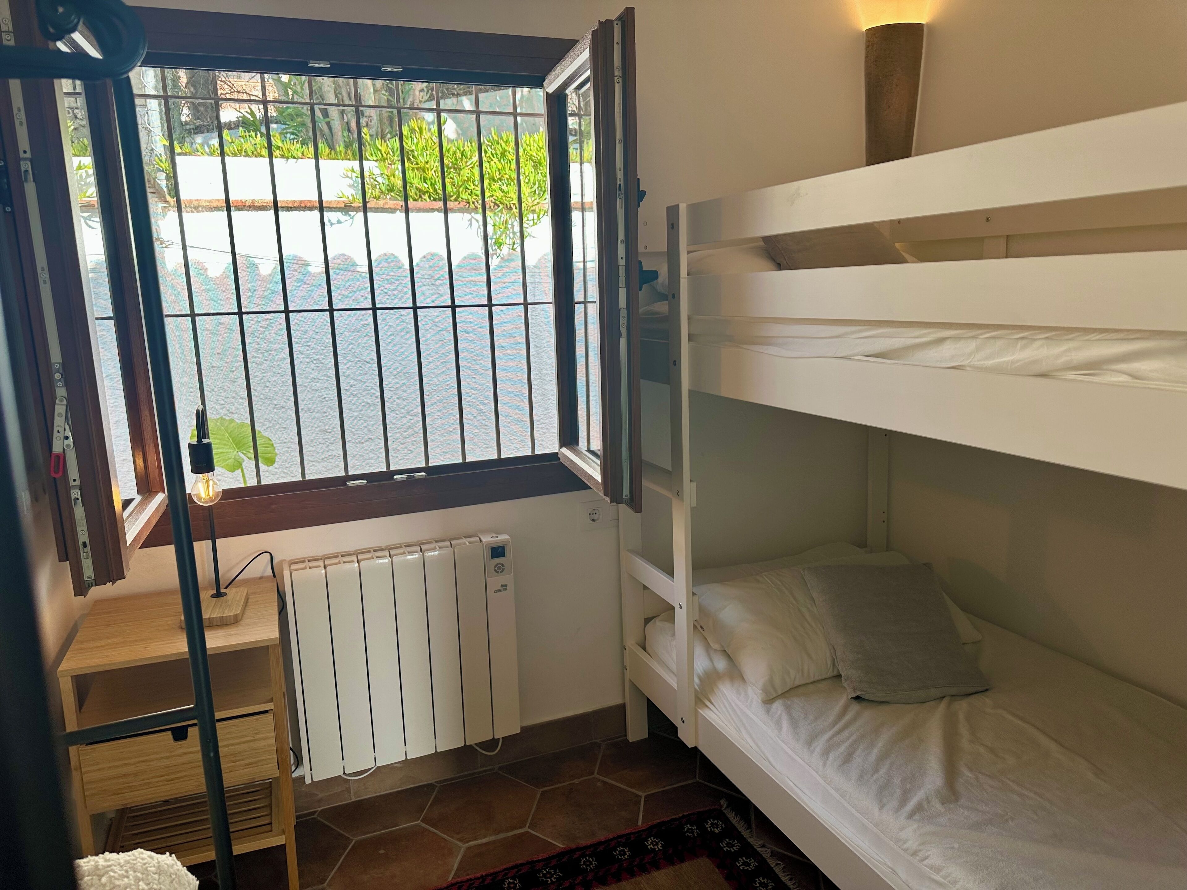 A bunk bed room with a window, radiator, and a wooden desk.