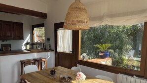 A wooden dining table with chairs, a hanging woven light fixture, and a view of a garden through a window.