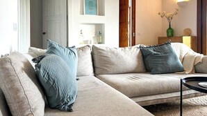 A living room with a beige sofa, two blue pillows, a small round table, and a wooden door.
