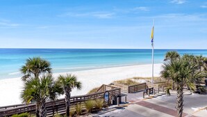 A beach with a wooden walkway, palm trees, and a flagpole. - Luxury Home + Carriage House - Heated Pool Oasis (Santa Rosa Beach)
