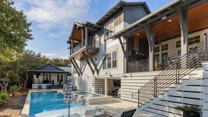 A two-story house with a swimming pool, outdoor seating, and a covered patio area. - Luxury Home + Carriage House - Heated Pool Oasis (Santa Rosa Beach)