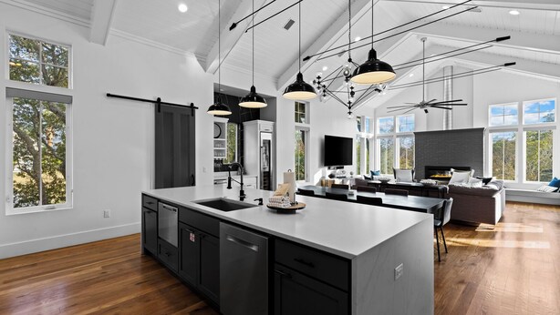 A modern kitchen with a large island, black cabinets, and pendant lighting. - Luxury Home + Carriage House - Heated Pool Oasis (Santa Rosa Beach)