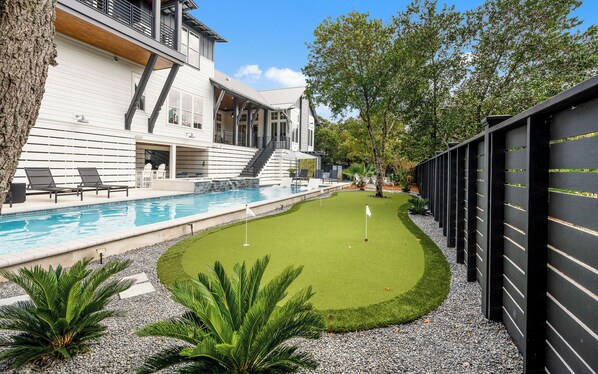 Une maison moderne dotée d’une piscine, d’une petite pelouse et d’un court de tennis.