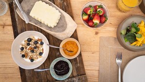 Une table dressée pour le petit-déjeuner, avec une variété d’aliments, notamment du yaourt agrémenté de granola, un bol de fraises, un bol de confiture d’orange et des œufs brouillés aux herbes.