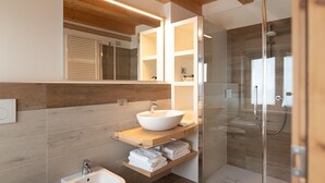 Une salle de bain moderne avec un grand miroir, un lavabo sur colonne, une cabine de douche et des éléments décoratifs en bois.