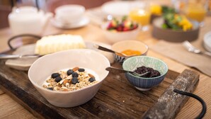 Ein Frühstückstisch mit Schüsseln voller Granola, Joghurt und Beeren, dazu Obstsalat und Orangensaft.