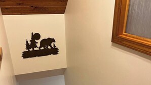 A wooden staircase with a rustic design, a wooden handrail, and a wall decal of a bear and trees. - Prime Snowmobile-Friendly Villa in Northern Maine  Winter Trails & Comfort (Bridgewater)