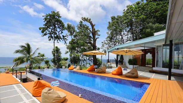 Un espace piscine doté d’une terrasse en bois, de chaises longues et de parasols.