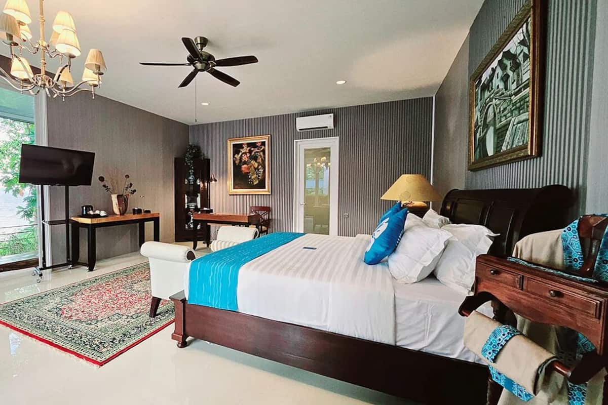 Un dormitorio con una cama grande, ventilador de techo, televisor y vistas al exterior.