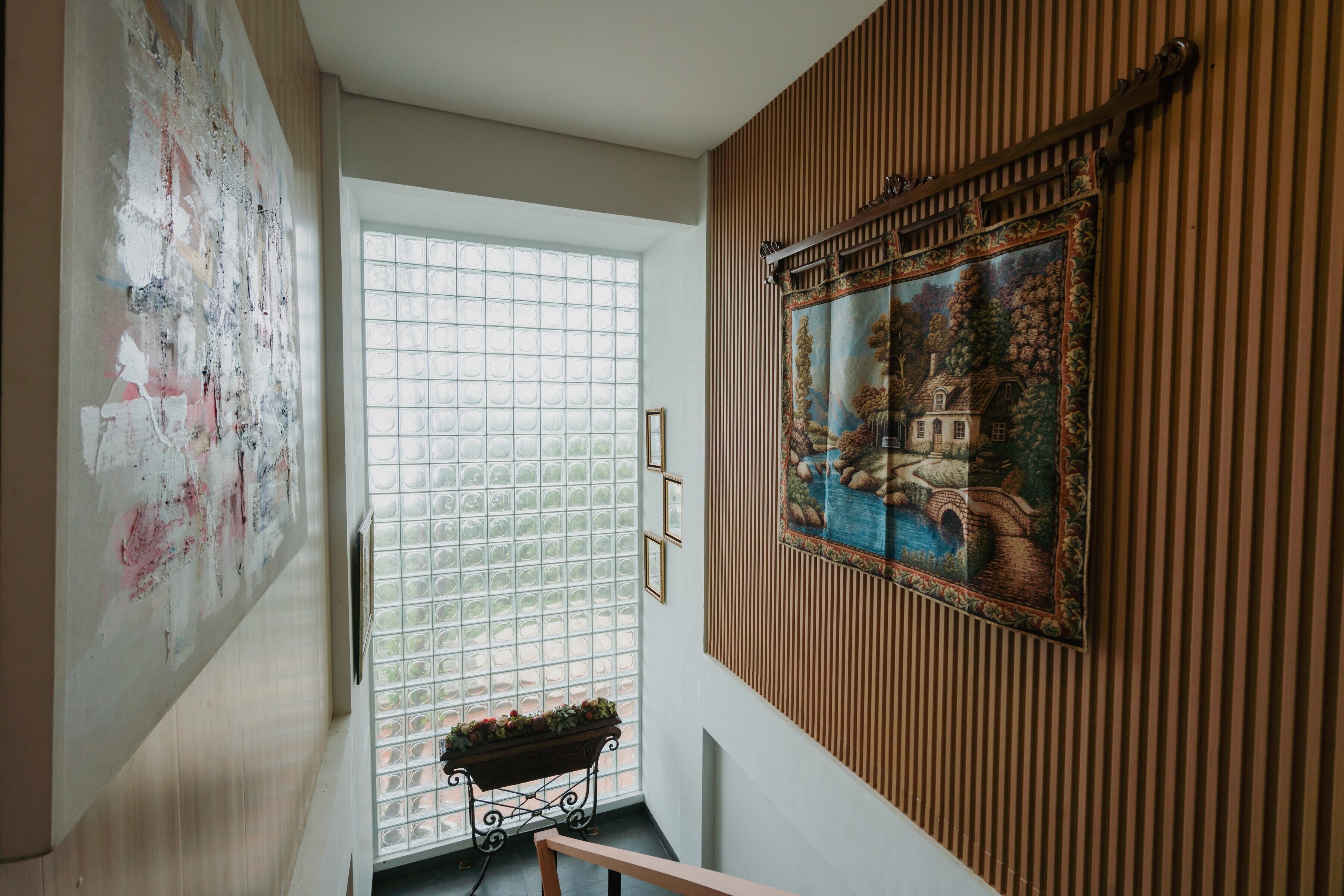 A room with a large abstract painting, a framed landscape painting, and a window with a view of a garden.