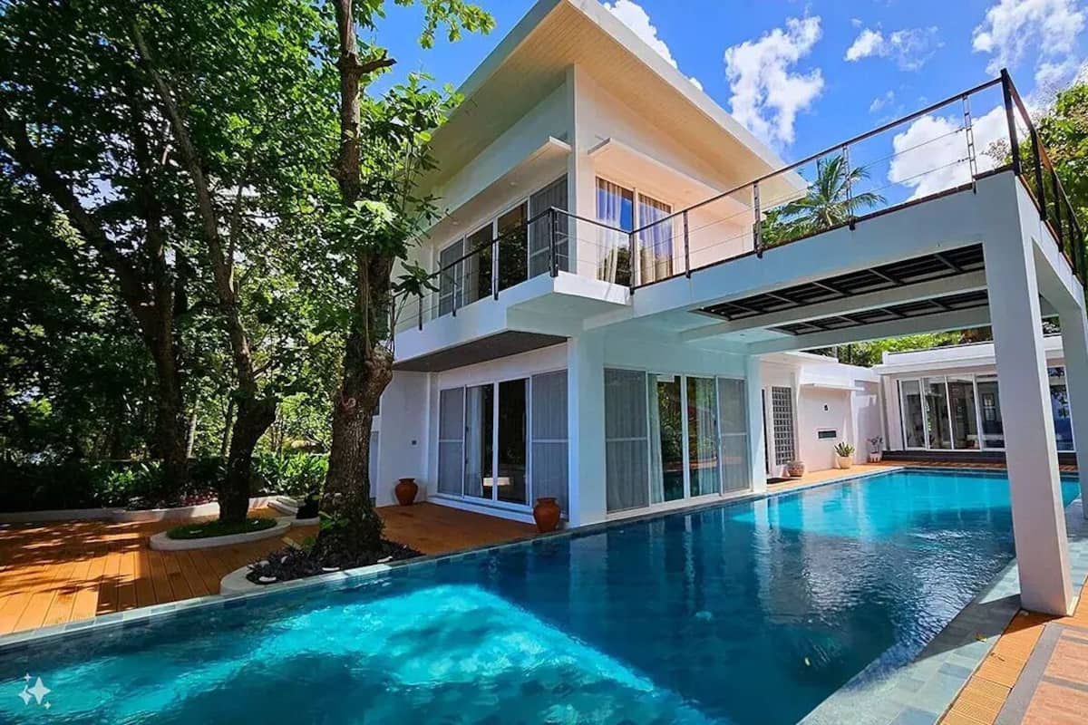 Una casa moderna de dos pisos con piscina, rodeada de abundante vegetación.