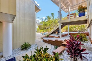 Une maison moderne dotée d’un espace extérieur couvert, d’un escalier et de diverses plantes.